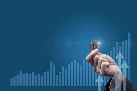 The concept of investing in bitcoins. Businessman shows Bitcoin against the background of a financial growth chart.の写真素材