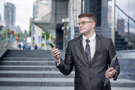 Young businessman with a mobile phone in his hands against the backdrop of a business center.の写真素材