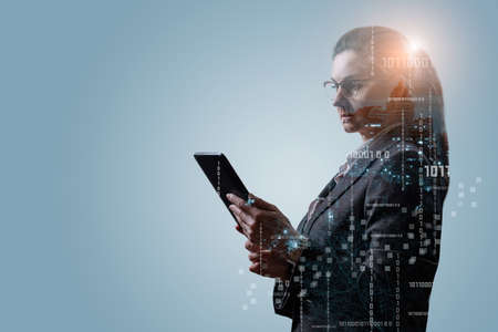 A woman in a business suit works on a tablet with binary codes on a blue background.の写真素材