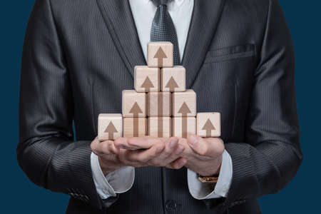 business profit growth concept. Businessman showing a pyramid of cubes with growth arrows.の写真素材