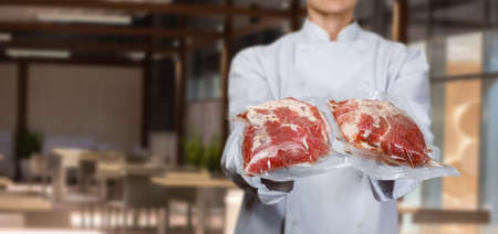 The cook shows the meat packed vacuum packaging on a blurred background.の写真素材