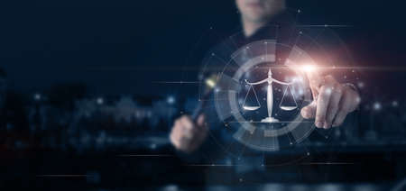 A lawyer with a judge gavel in his hands clicks on the scales of justice on a virtual screen.の写真素材