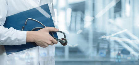 A doctor with documents and a stethoscope stands on a blurred background.の写真素材