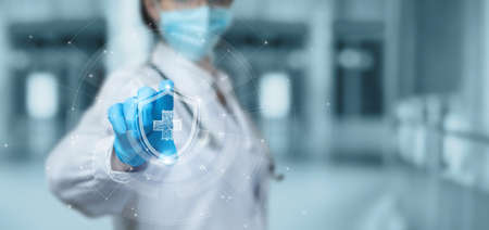 The concept of protecting health with the help of modern technologies. Doctor shows a shield with a cross on a virtual computer interface.の写真素材