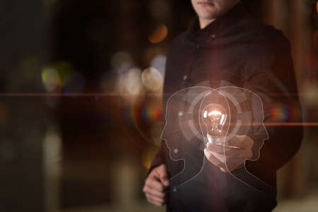 Idea concept of business psychology and teamwork. Businessman shows a burning light bulb against the background of the contours of workers.の写真素材