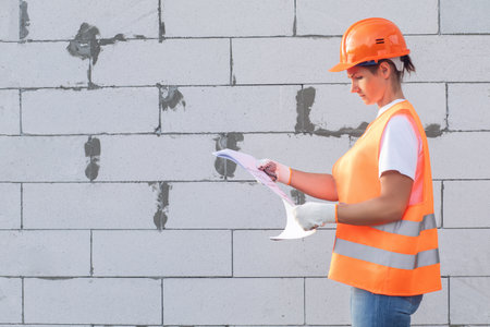 Builder in uniform studying the project against the background of a gas block wall.の写真素材
