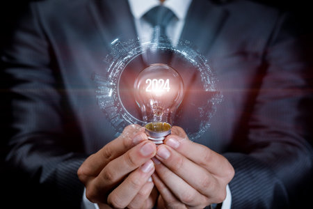 Concept of new ideas in the new year 2024. A man holds a light bulb with the glowing number 2024.の写真素材