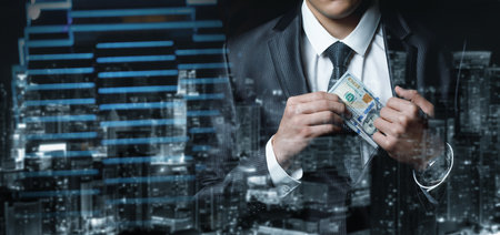 Businessman hides dollar bills in suit jacket against night city background.の写真素材