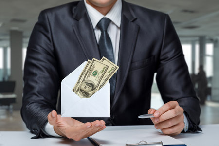 A businessman shows an envelope with dollars on a blurred office background.