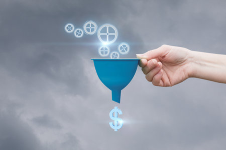 Sales funnel concept. A hand holds a funnel with a control mechanism at the entrance and a dollar at the exit.の写真素材