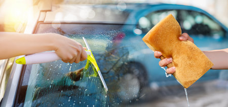 The concept of car washing and cleaning. Hands with a washcloth and a glass scraper wash a car.の写真素材