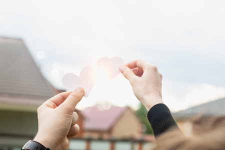 A couple shows hearts against the backdrop of a sunset between houses.の写真素材
