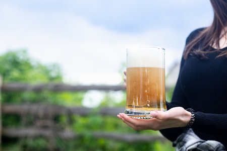 Girl holding a glass of beer, but with a blurred background of the village.