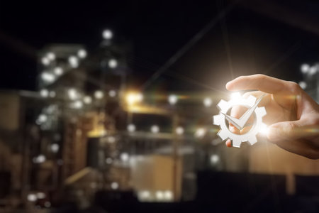 Concept of a quality production association or plant. While showing a gear with a check mark on a blurred background of a factory.の写真素材