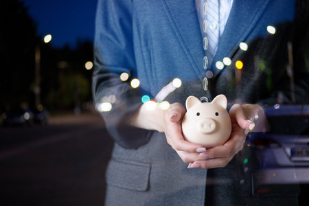 Woman in a business suit with a piggy bank in front of a city at night.の写真素材