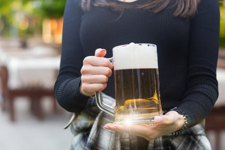Girl holding a glass of beer on a blurred background. Girl enjoying a cool glass of beer outdoors.の写真素材