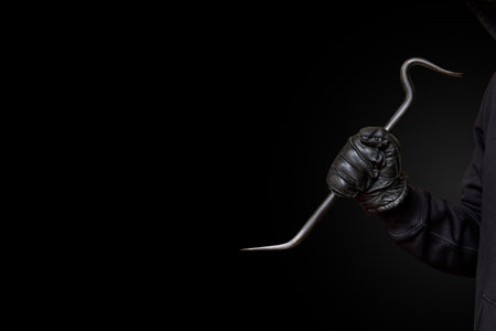 The concept of the danger of hacking. A thief holds a crowbar in his hands on a black background.の写真素材