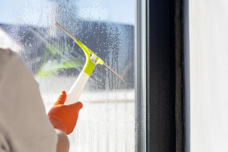 A cleaning lady cleans a window with a scraper. The concept of cleaning and washing windows.の写真素材