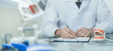 Dental precision Documenting health. A dentist in a professional uniform fills out a patient registration log against the background of a modern clinic.の写真素材
