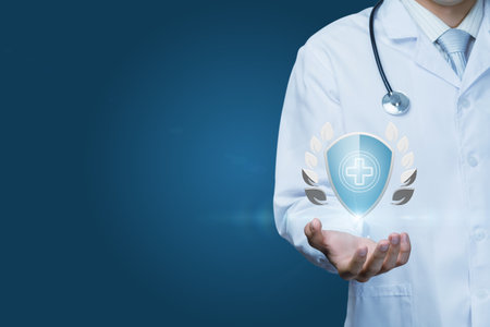A healthcare worker wearing a white coat holds a holographic shield symbol that represents health and safety. The background is a calming blue, emphasizing professionalism and care.の写真素材