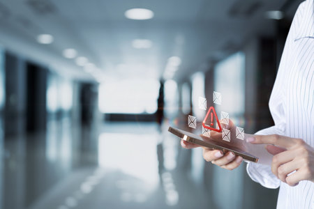 A person interacts with a smartphone displaying alerts and notifications. The modern setting features a blurred background of a sleek high tech environment.の写真素材