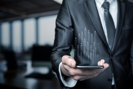 A business professional in formal attire holds a smartphone showing dynamic graphical data emerging from the device.の写真素材