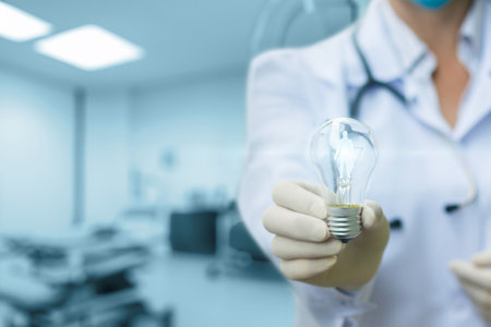 A healthcare professional holds a light bulb in a modern examination room, symbolizing innovative ideas in patient care and diagnostics. The background shows medical equipment.の写真素材