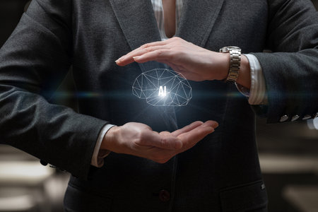 A man in a gray suit holds a holographic representation of a brain, symbolizing artificial intelligence, while showing innovative technology. The setting suggests a business or tech environment.の写真素材