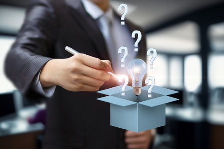 A professional in a suit is brainstorming ideas by drawing lightbulbs and question marks above a box. This scene showcases innovation and problem-solving in a collaborative office environment.の写真素材