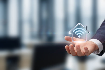 A person holds a glowing home icon with a Wi-Fi symbol, representing innovation in smart home technology within a contemporary office space. The background suggests a busy work environment.の写真素材