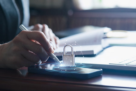 A person using a stylus on a smartphone while focusing on digital security. Nearby, a laptop and...