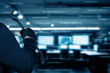 A figure holding a crowbar stands in a dimly lit office filled with computer screens. The atmosphere is tense, suggesting potential harmful activity.の写真素材