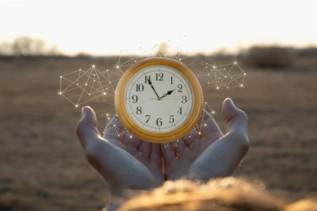 A person holds a vintage clock under a clear sky, with digital sparks surrounding it. The sunlight casts a warm glow, enhancing the sense of time's significance in an open field.の写真素材