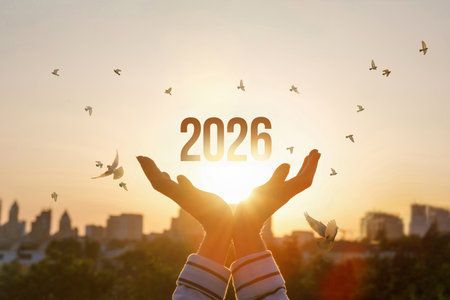 Hands raised to the sky to celebrate the arrival of 2026 as sunlight casts a warm glow, while birds...