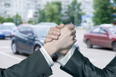 Handshake in the city while cars pass by in the background. Two individuals engage in a firm handshake amidst a busy street urban filled with vehicles.の写真素材