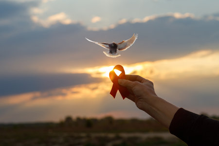 Hope and freedom at sunset with a red ribbon and dove. A person holds a red ribbon while a dove...