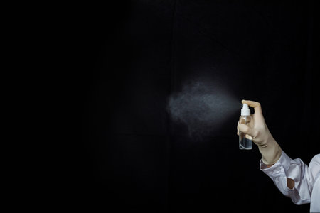 Spraying a fine mist of liquid. A person in gloves is spraying a clear liquid into the air against a dark backdrop.の写真素材