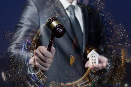 Real estate auction at night. A man in a suit holds a gavel and a small house model during a nighttime auction event.の写真素材