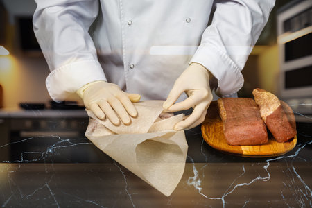 A skilled chef wraps fresh ingredients with care in a modern kitchen setting.の写真素材