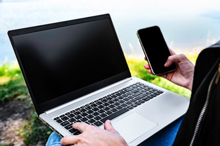 A young freelance woman working outdoors with laptop and mobile phone sitting in nature. Concept of...