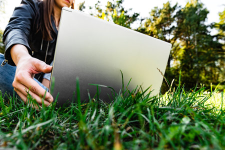 Young female freelancer working on laptop computer sitting on field of green grass on sunny day.の写真素材