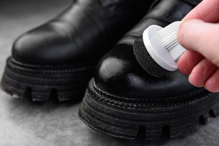 Female's hands taking care of leather shoes on gray background.の写真素材