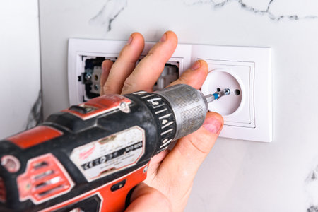 Installing outlet on white tile wall using electric screwdriver.
