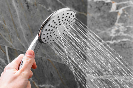 Hand holding shower head on shower room background.