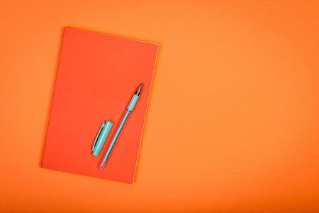Orange notebook and pen on orange background.の写真素材