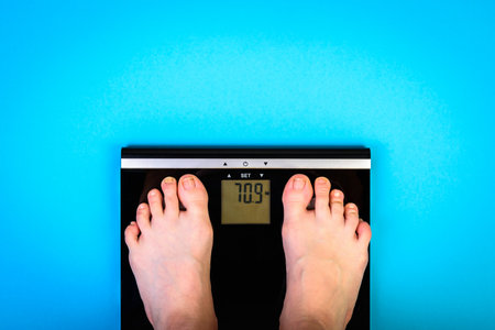 Woman's feet standing on digital weight scale on blue background.の写真素材