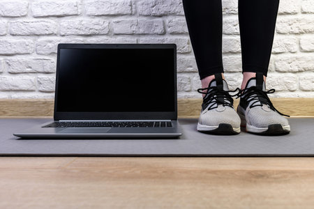 Sporty woman in sportswear is standing with laptop on the floor at home in the living room.