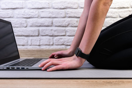 Sporty woman in sportswear is preparing for workout and is using a laptop at home in the living room.の写真素材