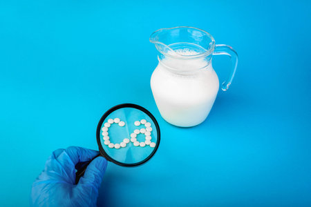 Hands in gloves searching for calcium in milk using magnifying glass on blue background.の写真素材