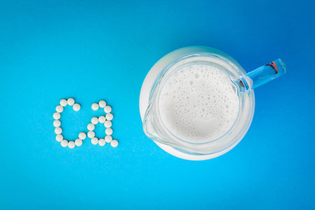 White pills forming shape to Ca alphabet and jug of milk on blue background.の写真素材
